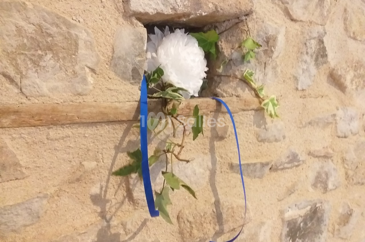 Fleur blanche et lierre avec un ruban bleu insérés dans une ouverture d'un mur en pierre.