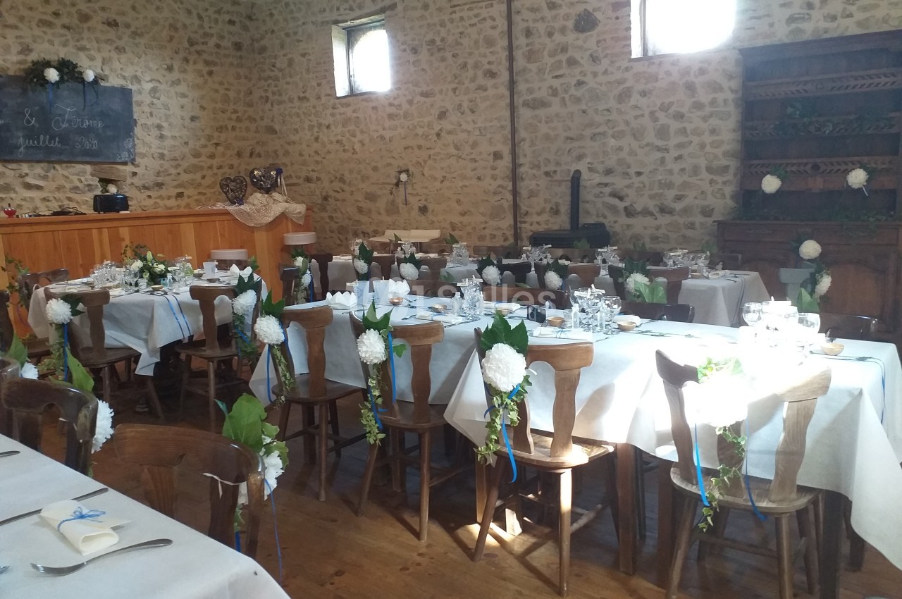 Salle de réception décorée pour un mariage, avec tables dressées, fleurs blanches et murs en pierre apparente.