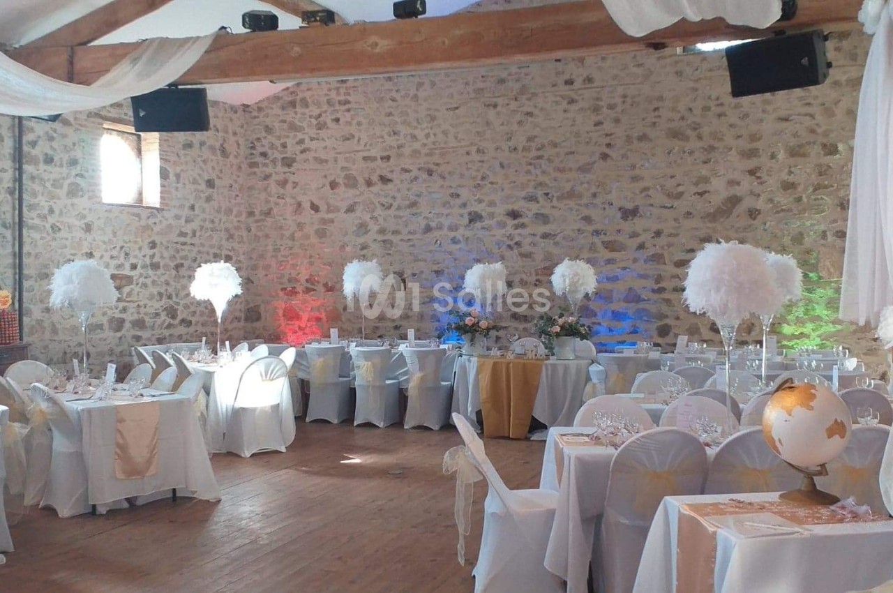 Salle de réception décorée avec des tables blanches, des centres de table en plumes et des murs en pierre apparente.