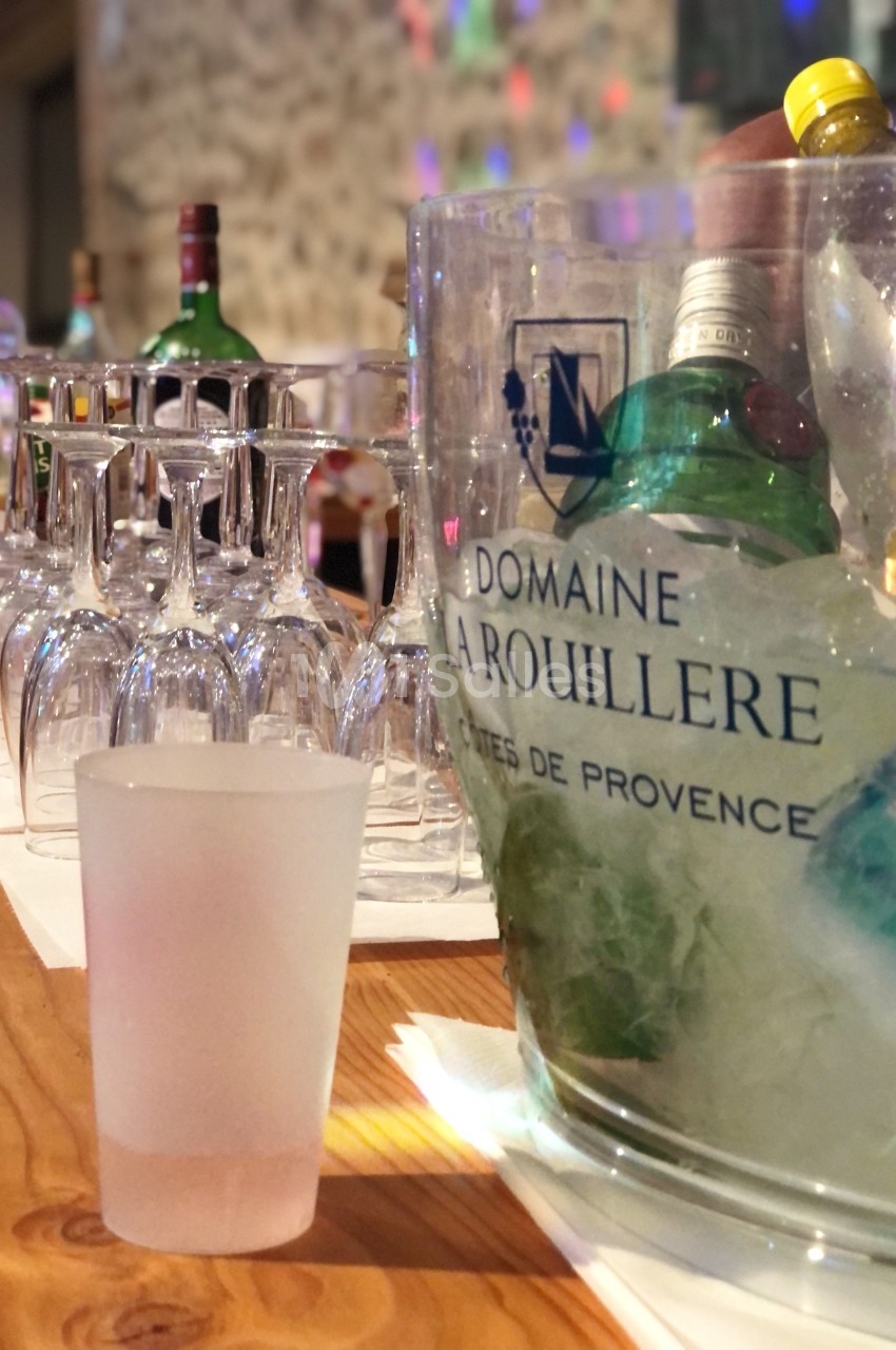 Seau rempli de glace contenant des bouteilles, aligné avec des verres à pied sur une table en bois.