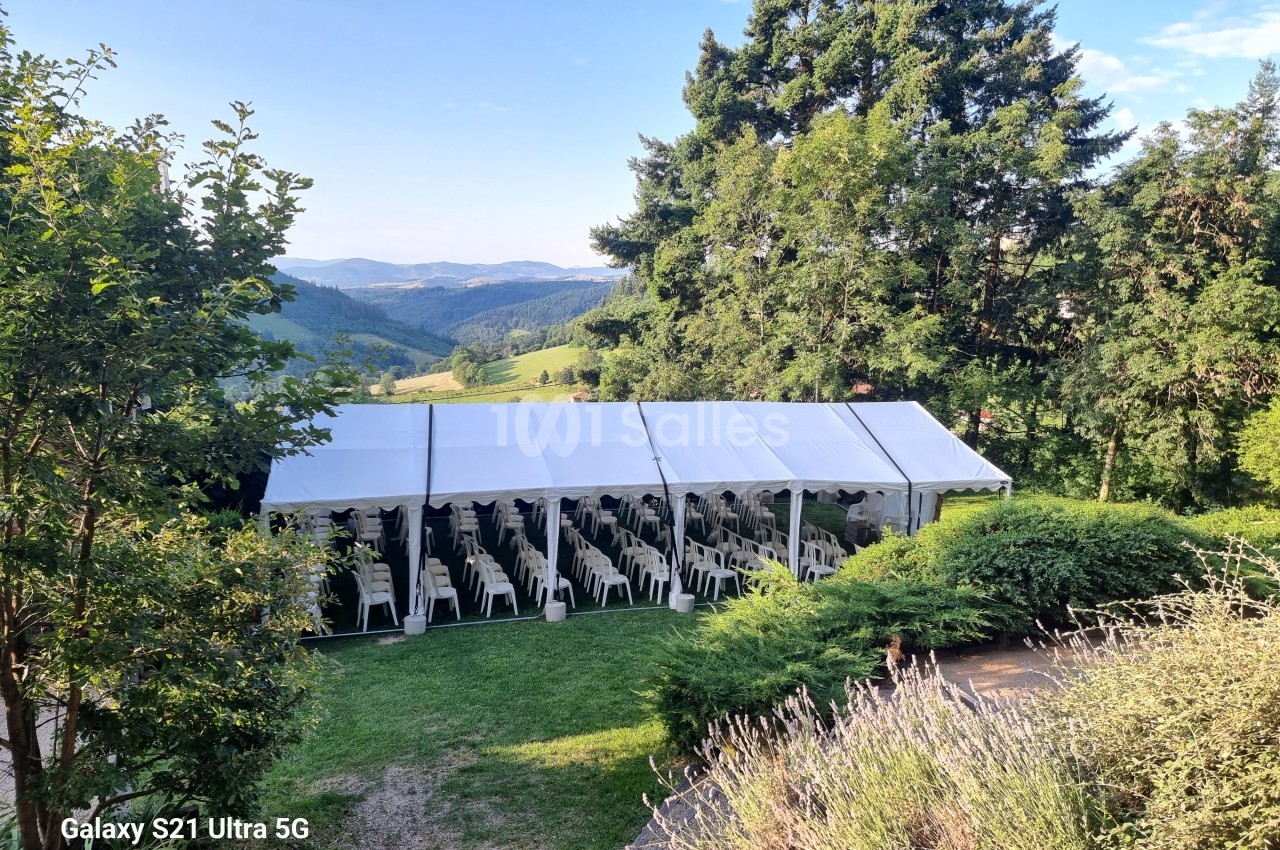 Grande tente blanche installée en extérieur, entourée de verdure, avec des rangées de chaises alignées à l'intérieur.