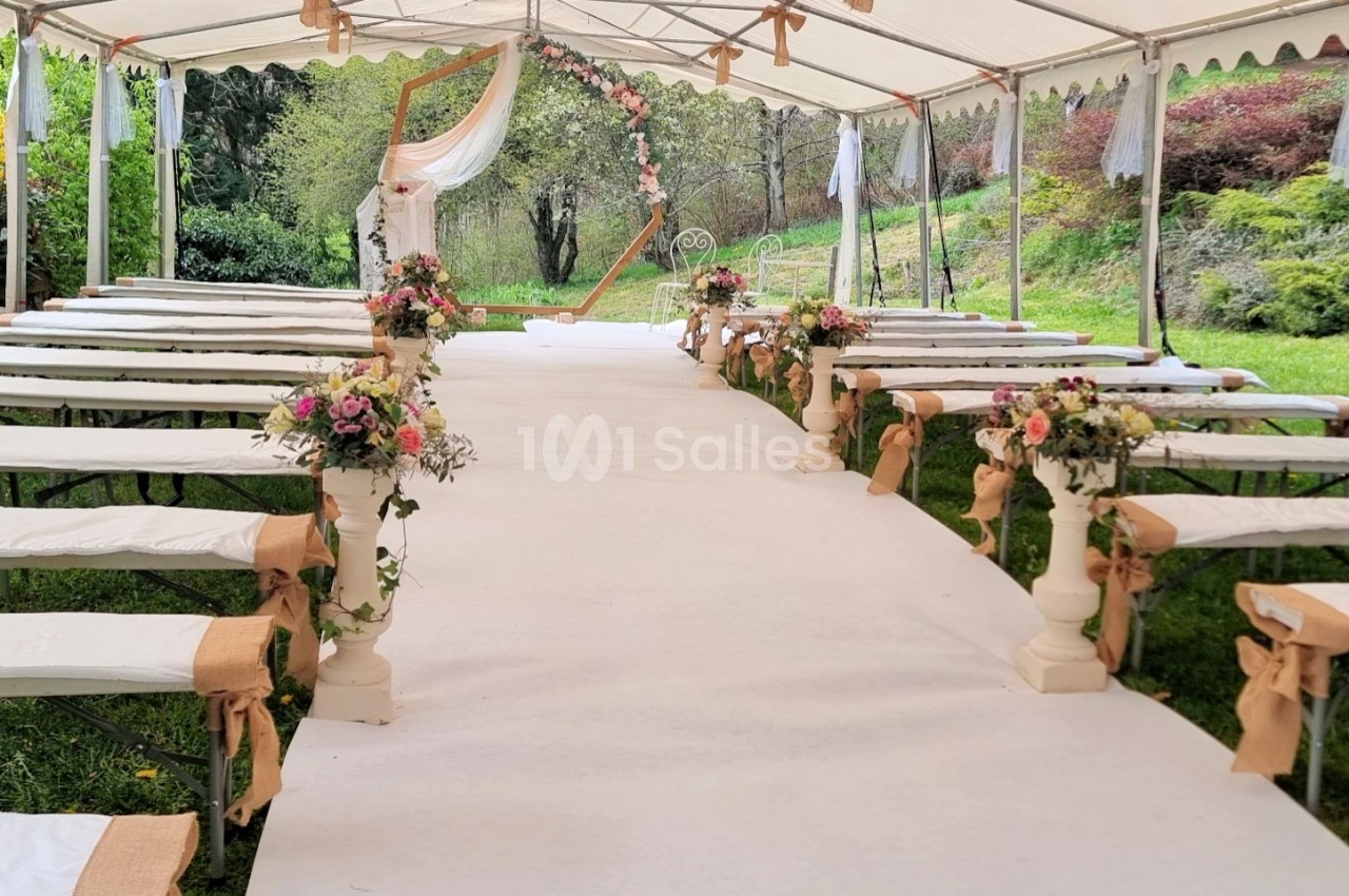 Allée centrale décorée de fleurs sous une tente blanche, préparée pour une cérémonie en extérieur.