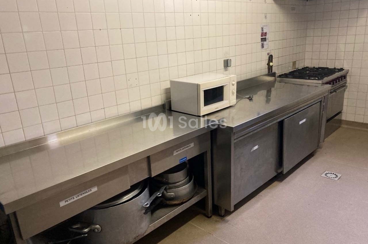 Cuisine professionnelle avec plan de travail en inox, micro-ondes, plaques de cuisson et équipements de rangement.