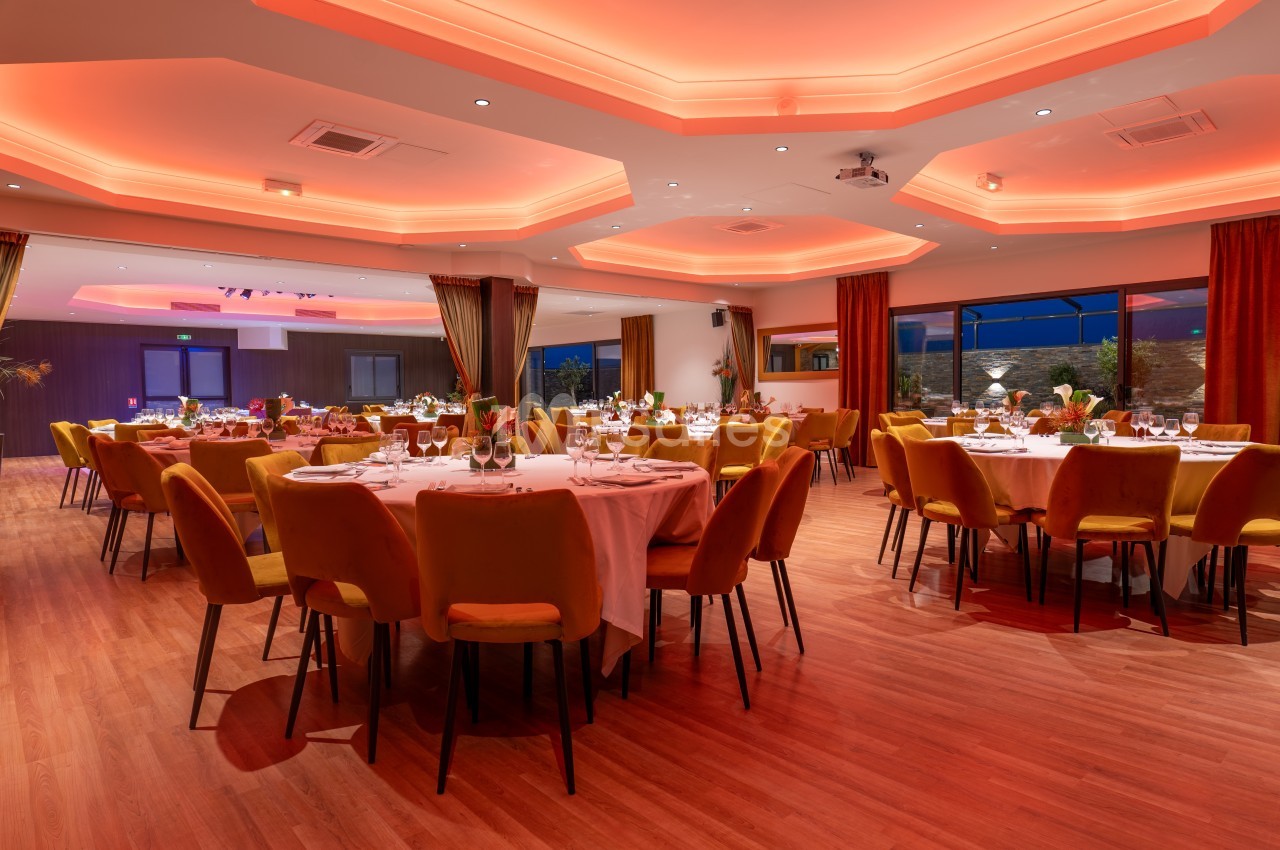 Salle de réception élégante avec tables rondes dressées, éclairage tamisé et grandes baies vitrées.