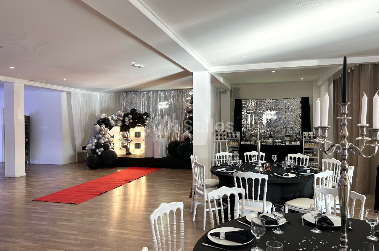 Salle décorée pour un événement avec tables dressées, tapis rouge et décor lumineux incluant le chiffre 18.
