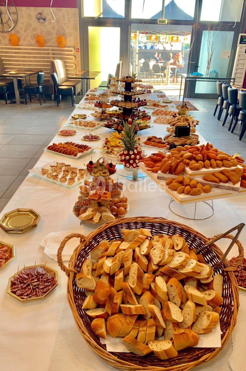 Table garnie d'un buffet varié comprenant pains, viennoiseries, charcuteries et desserts dans une salle lumineuse.