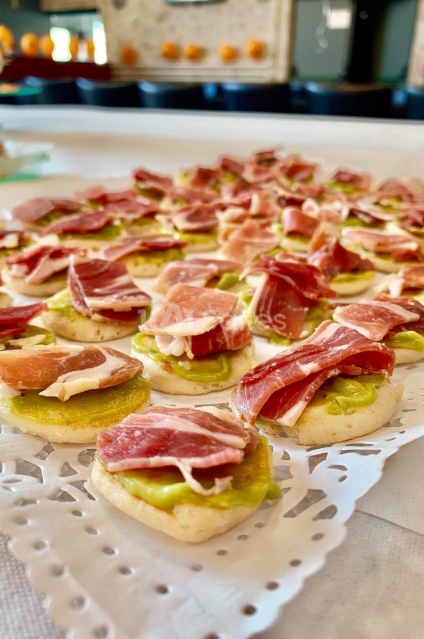 Assortiment de canapés garnis de jambon cru et d'une base de crème verte, disposés sur un plateau décoratif.