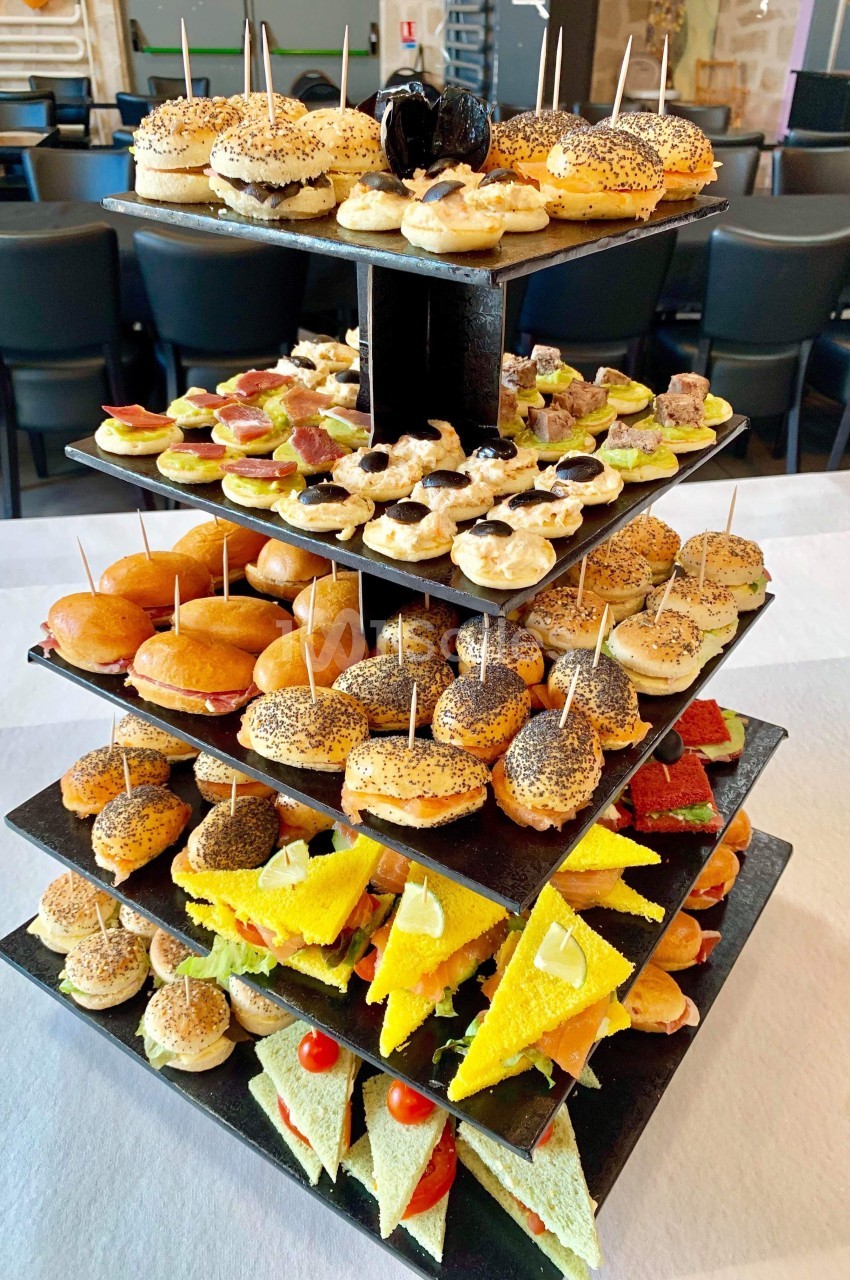 Plateau à étages présentant une variété de petits sandwichs et amuse-bouches colorés sur une table blanche.