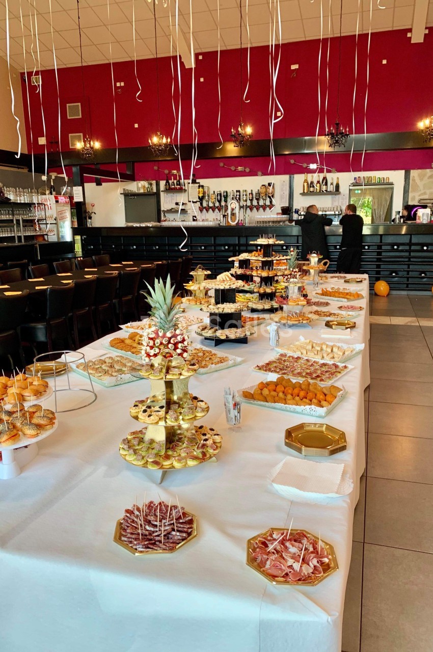 Buffet garni de plats variés sur une longue table blanche, dans une salle décorée avec des ballons suspendus.