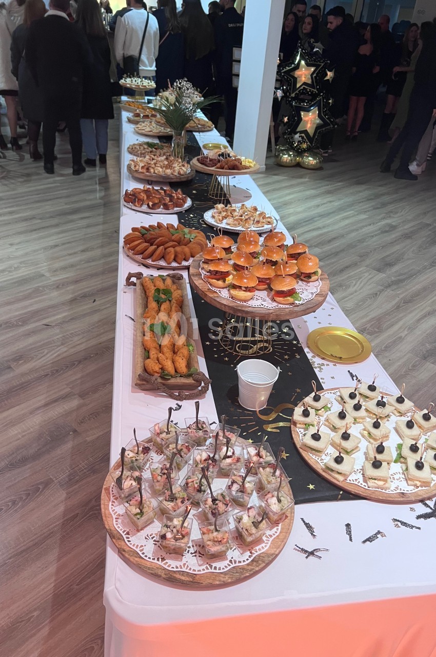 Table garnie de divers amuse-bouches et plats de fête, disposés pour un buffet dans une salle lumineuse.