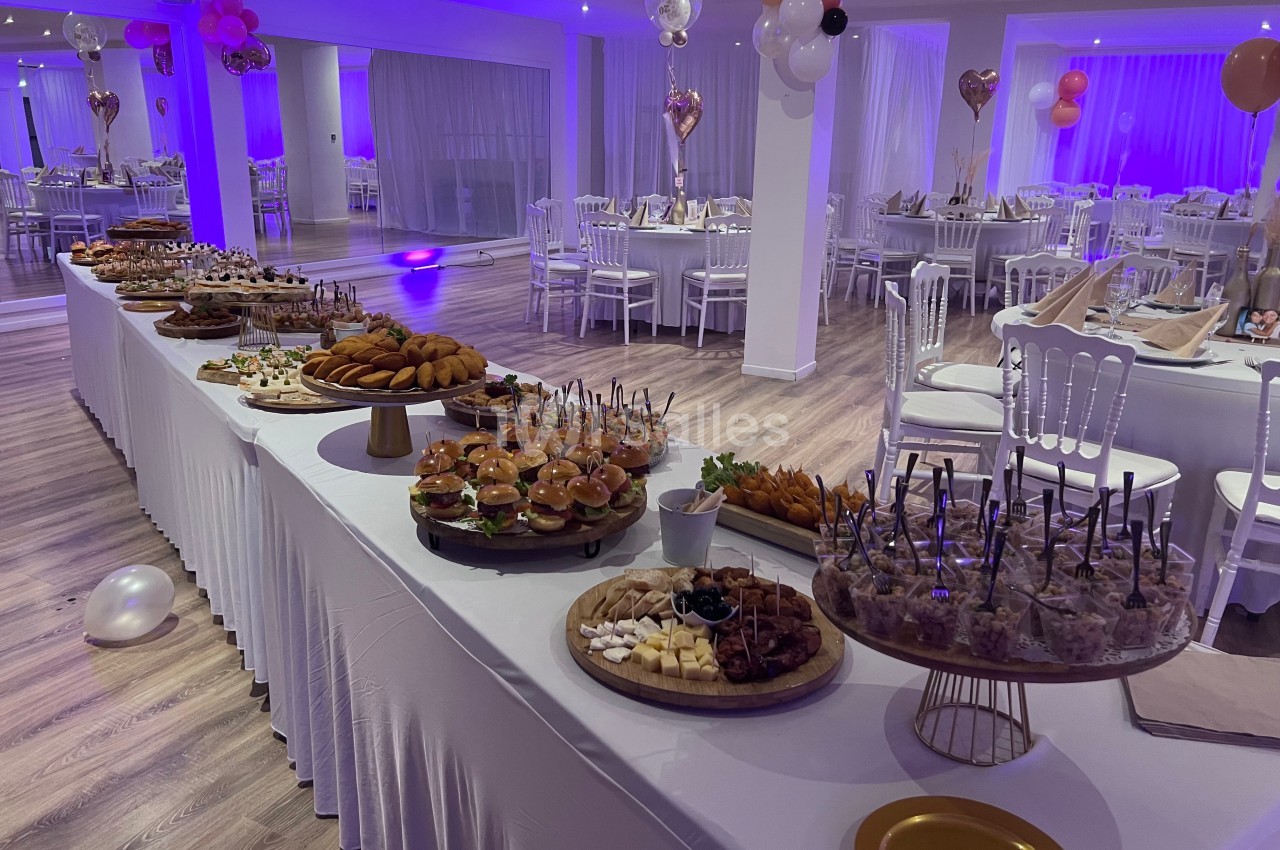 Buffet varié avec plats salés et sucrés, dans une salle décorée pour un événement festif avec tables dressées.