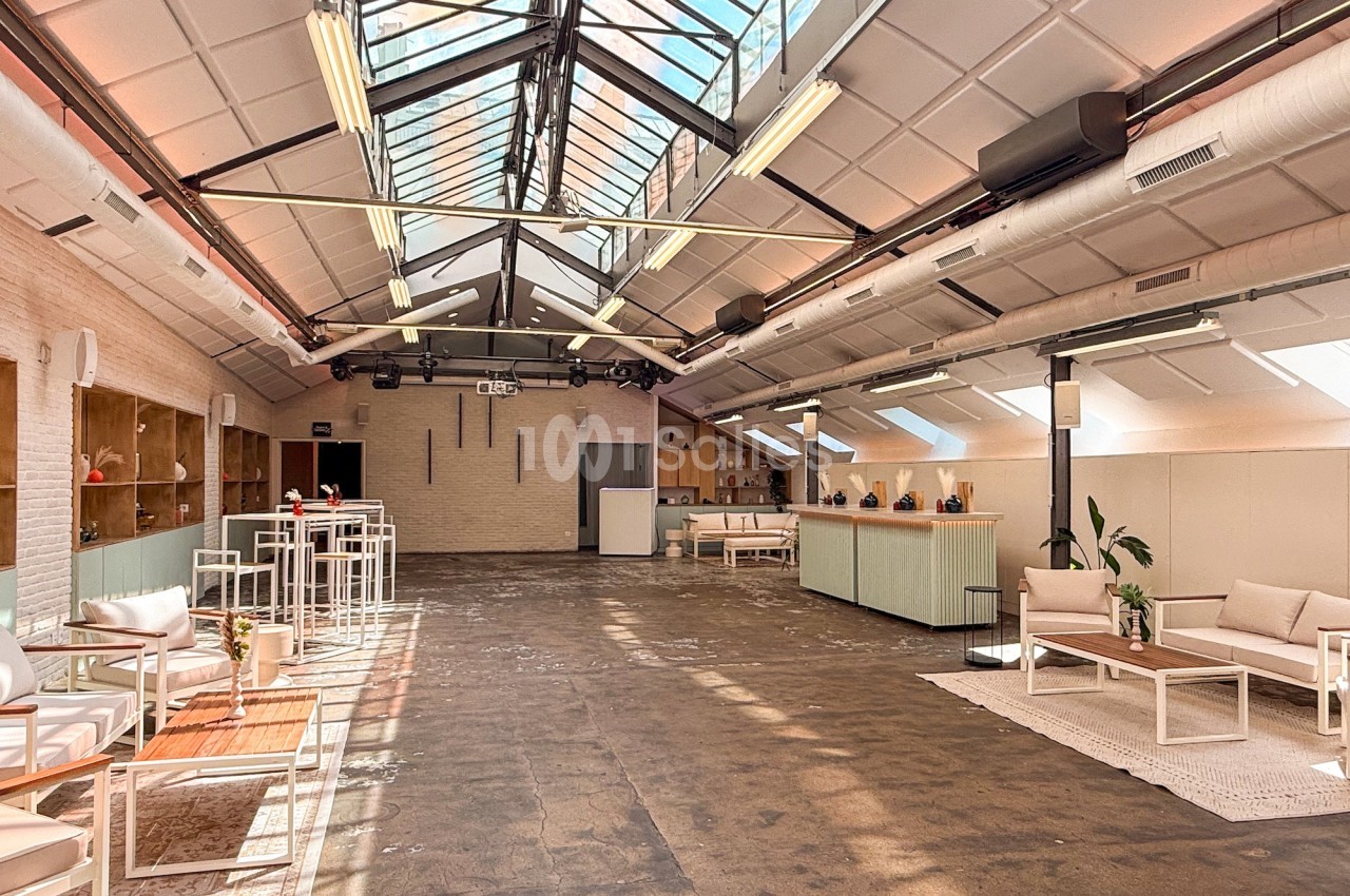 Salle lumineuse avec verrière, mobilier moderne et espace aménagé avec canapés, tables basses et comptoir d'accueil.