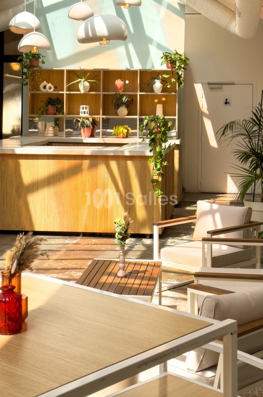 Intérieur lumineux d'un café moderne avec des plantes suspendues, un comptoir en bois et des fauteuils confortables.