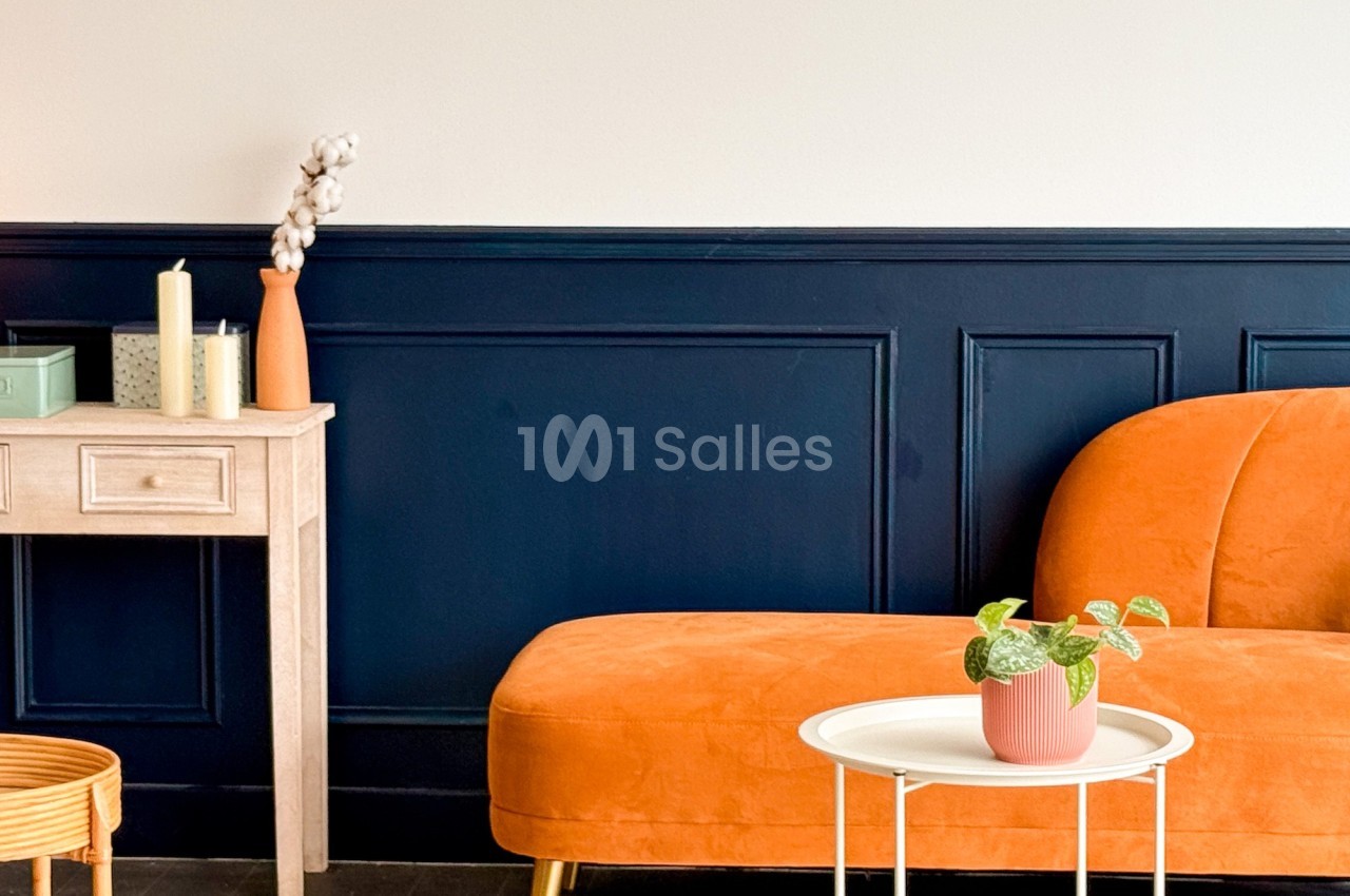 Canapé orange avec table basse blanche, plante en pot et console en bois clair contre un mur bleu et beige.