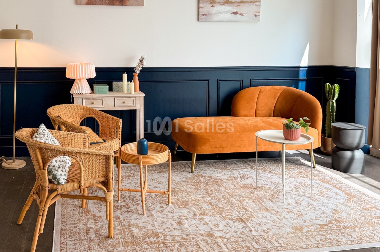 Salon lumineux avec canapé orange, fauteuils en rotin, tables basses, tapis beige et décoration murale.