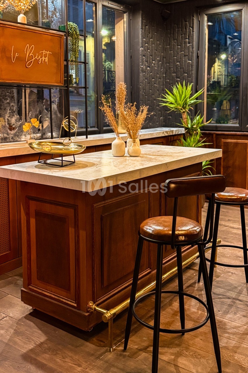 Comptoir en bois avec plateau en marbre, tabourets hauts et décoration végétale dans un espace intérieur chaleureux.