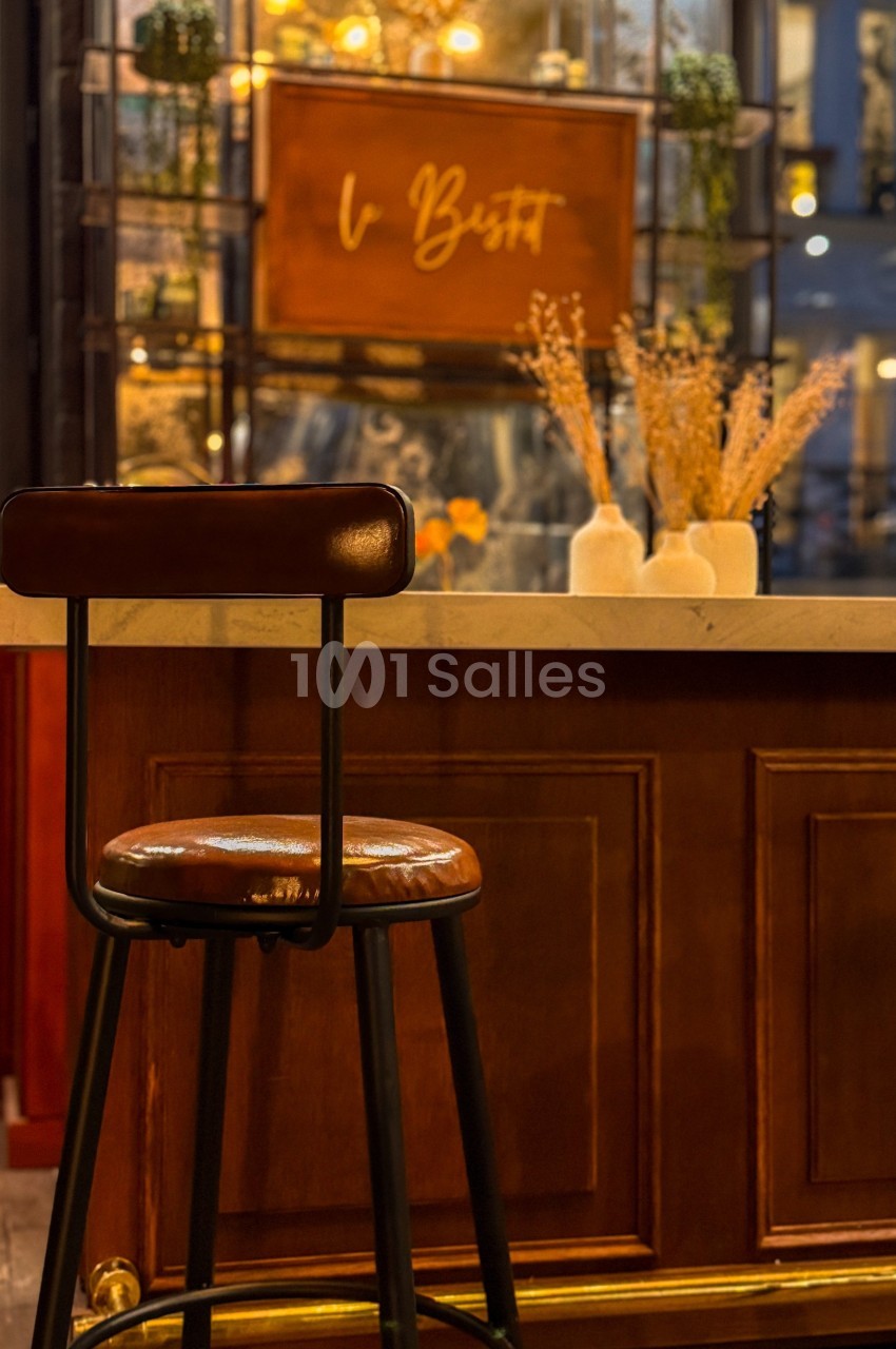Tabouret en cuir brun devant un comptoir en bois, avec des vases décoratifs et un panneau lumineux en arrière-plan.