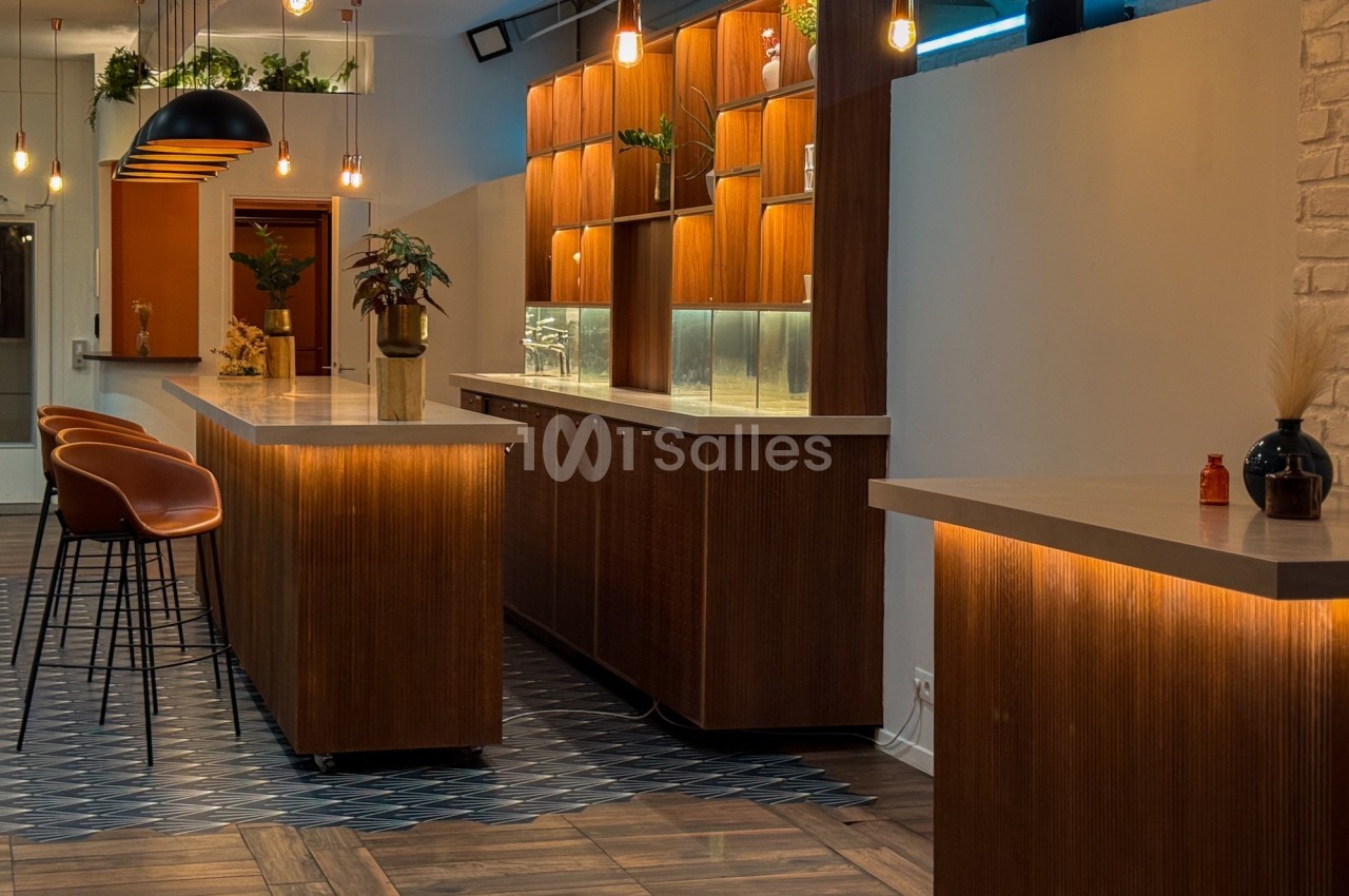 Intérieur d'un bar moderne avec comptoirs en bois, tabourets, éclairage suspendu et décorations végétales.