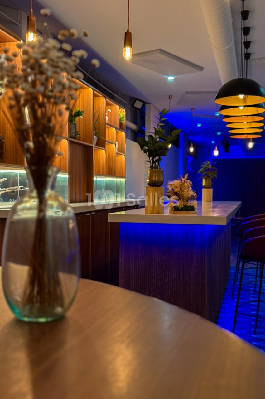 Espace intérieur moderne avec éclairage tamisé, comptoir en bois, étagères illuminées et décoration florale.
