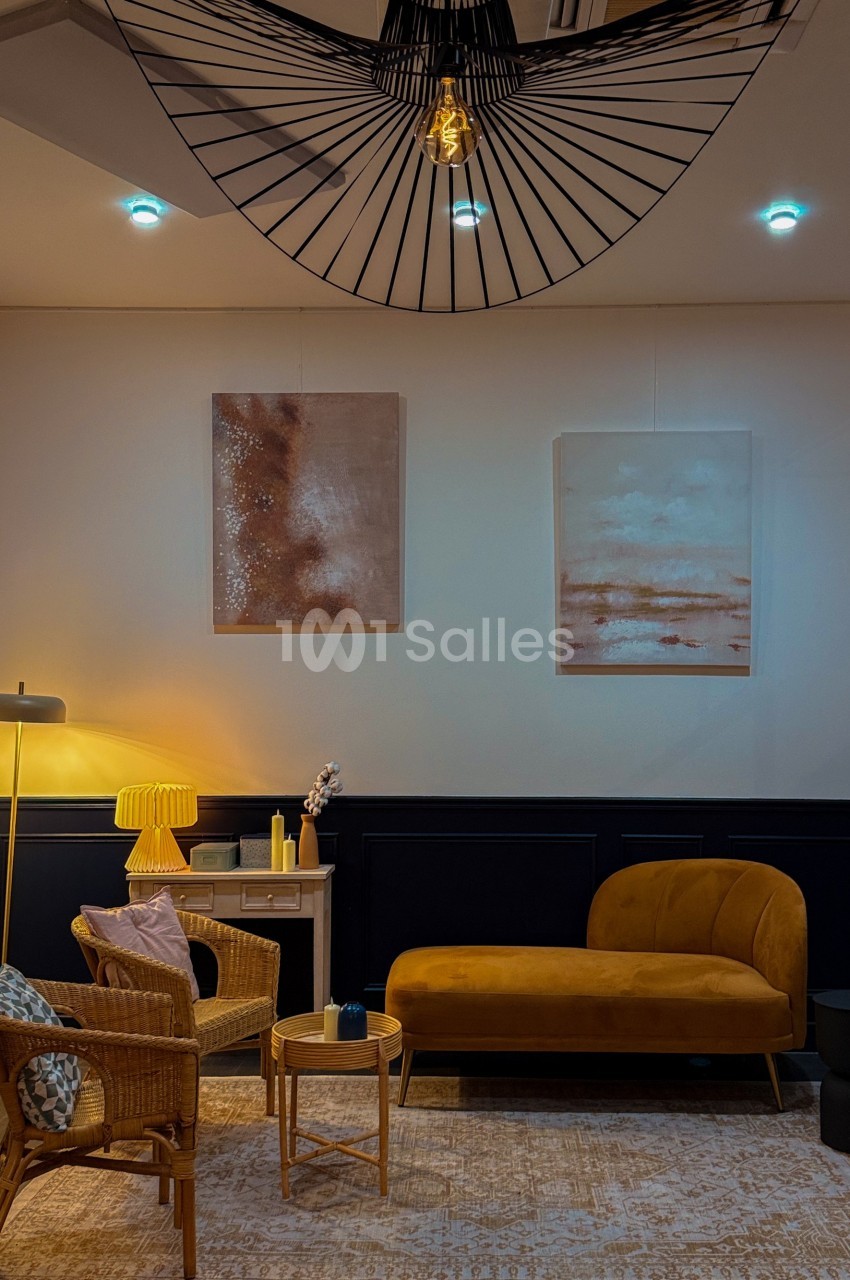 Salon moderne avec canapé jaune, fauteuils en rotin, table basse en bois, lampes et tableaux abstraits sur un mur clair.