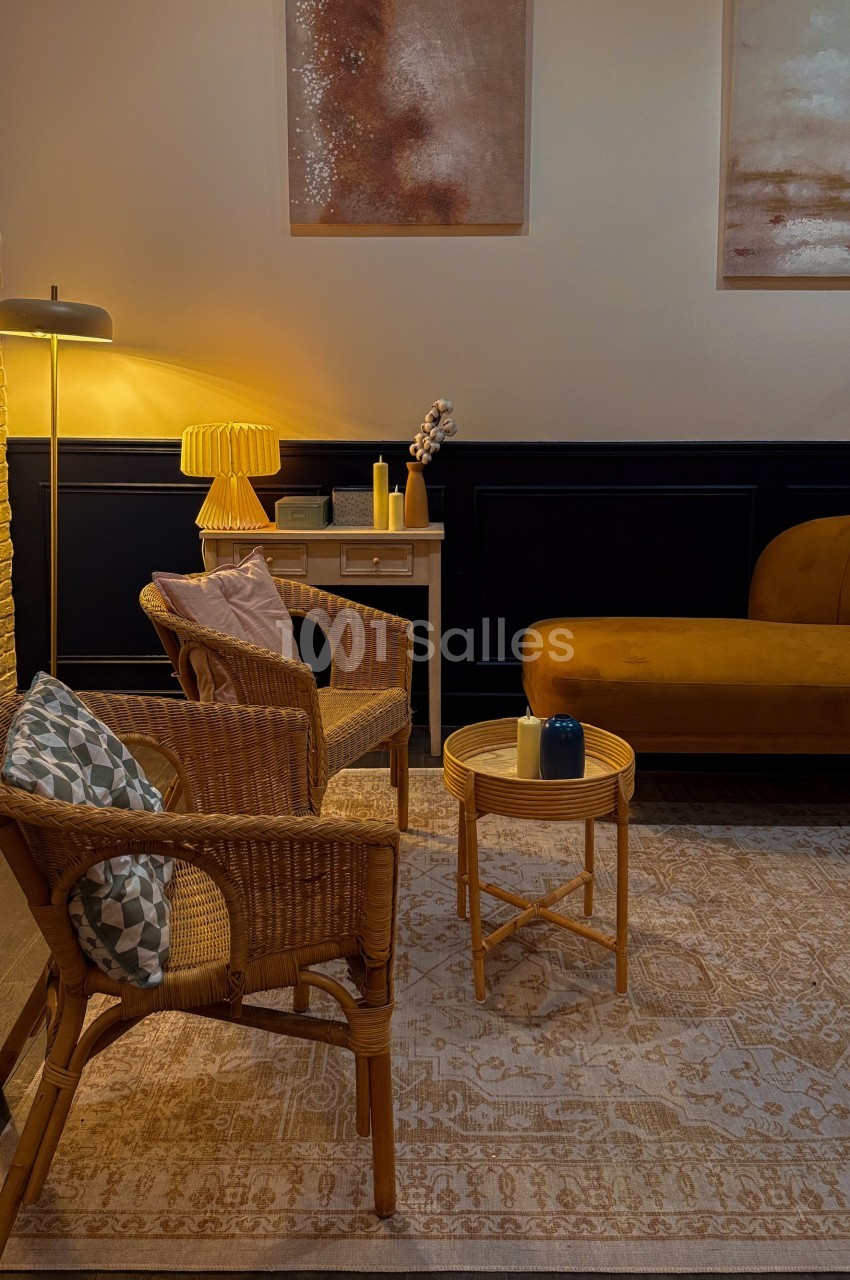 Espace salon chaleureux avec fauteuils en rotin, table basse, canapé jaune moutarde et éclairage tamisé.