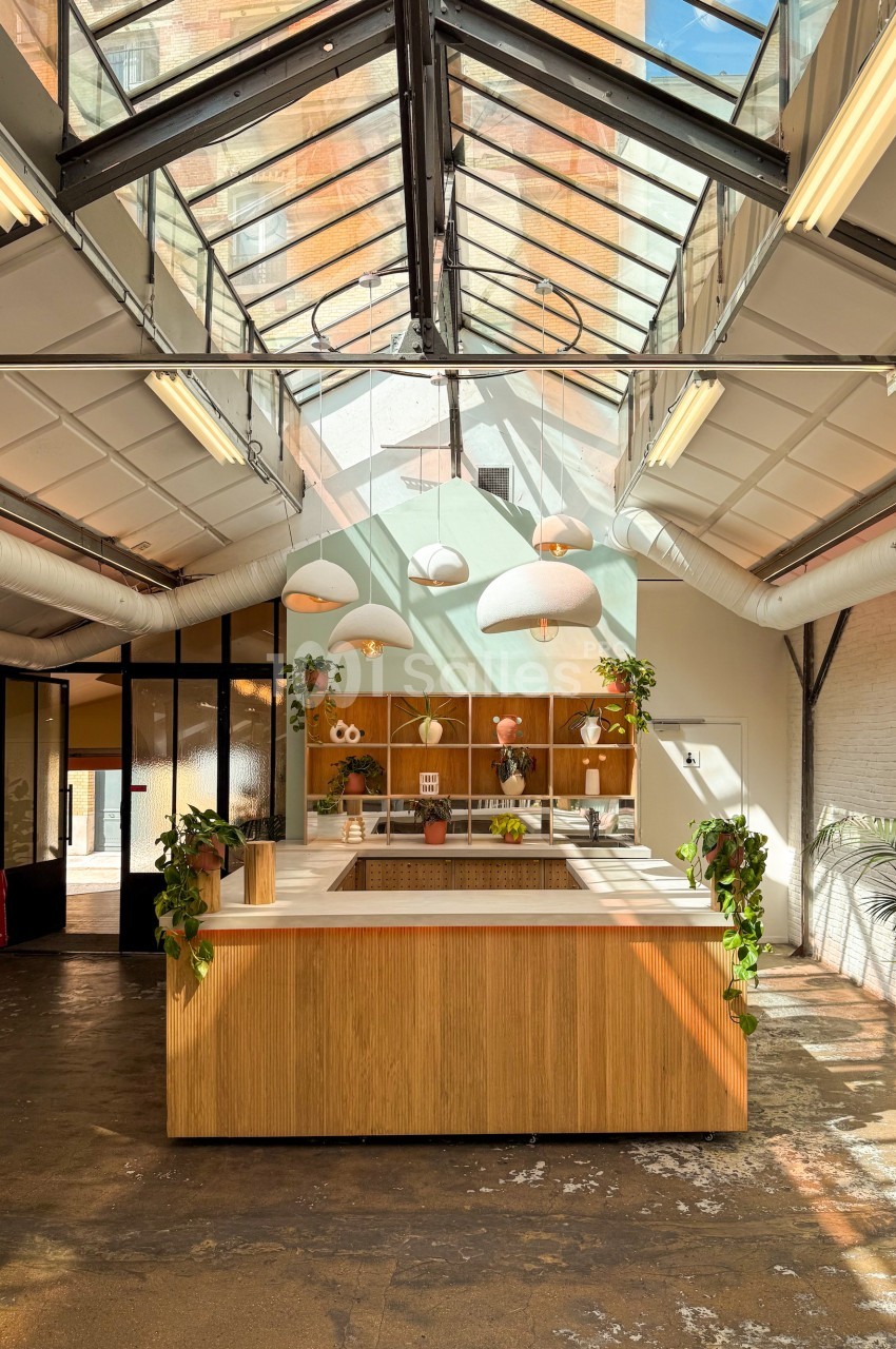 Cuisine moderne avec un îlot central en bois, éclairée par une verrière et des suspensions lumineuses.