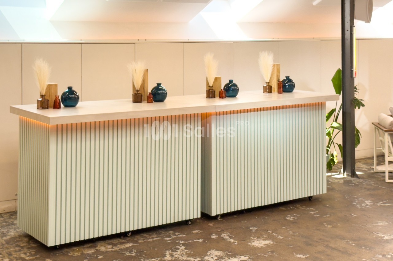 Comptoir moderne avec façade à lattes, décoré de vases bleus et dorés, dans un espace lumineux au sol en béton.