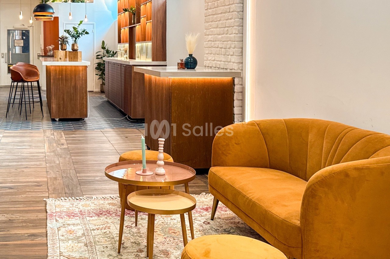 Espace lounge avec canapé jaune, table basse et décoration moderne, éclairé par des luminaires suspendus.