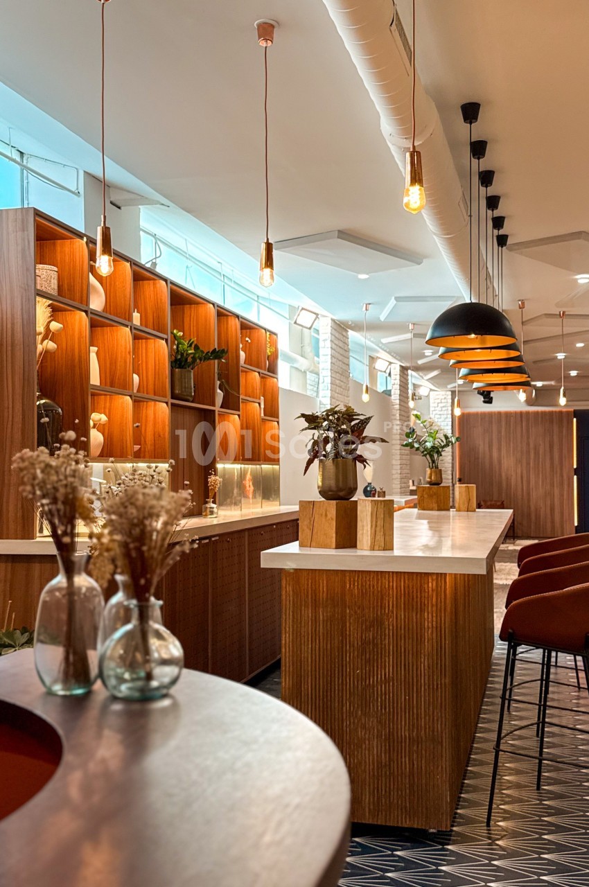 Espace intérieur moderne avec comptoirs en bois, étagères éclairées, suspensions design et chaises hautes.