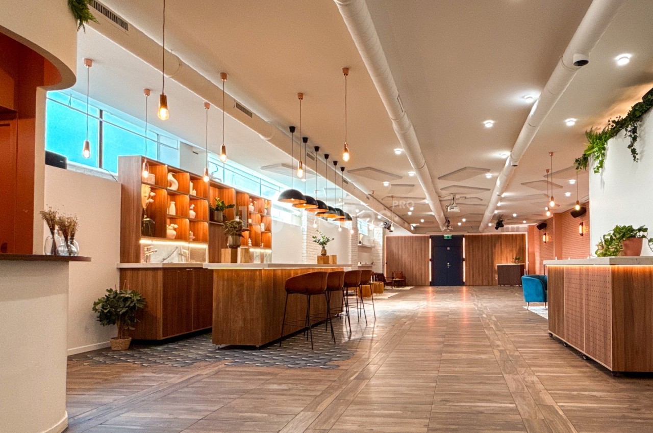 Espace intérieur moderne avec sol en bois, comptoirs en bois, suspensions lumineuses et plantes décoratives.