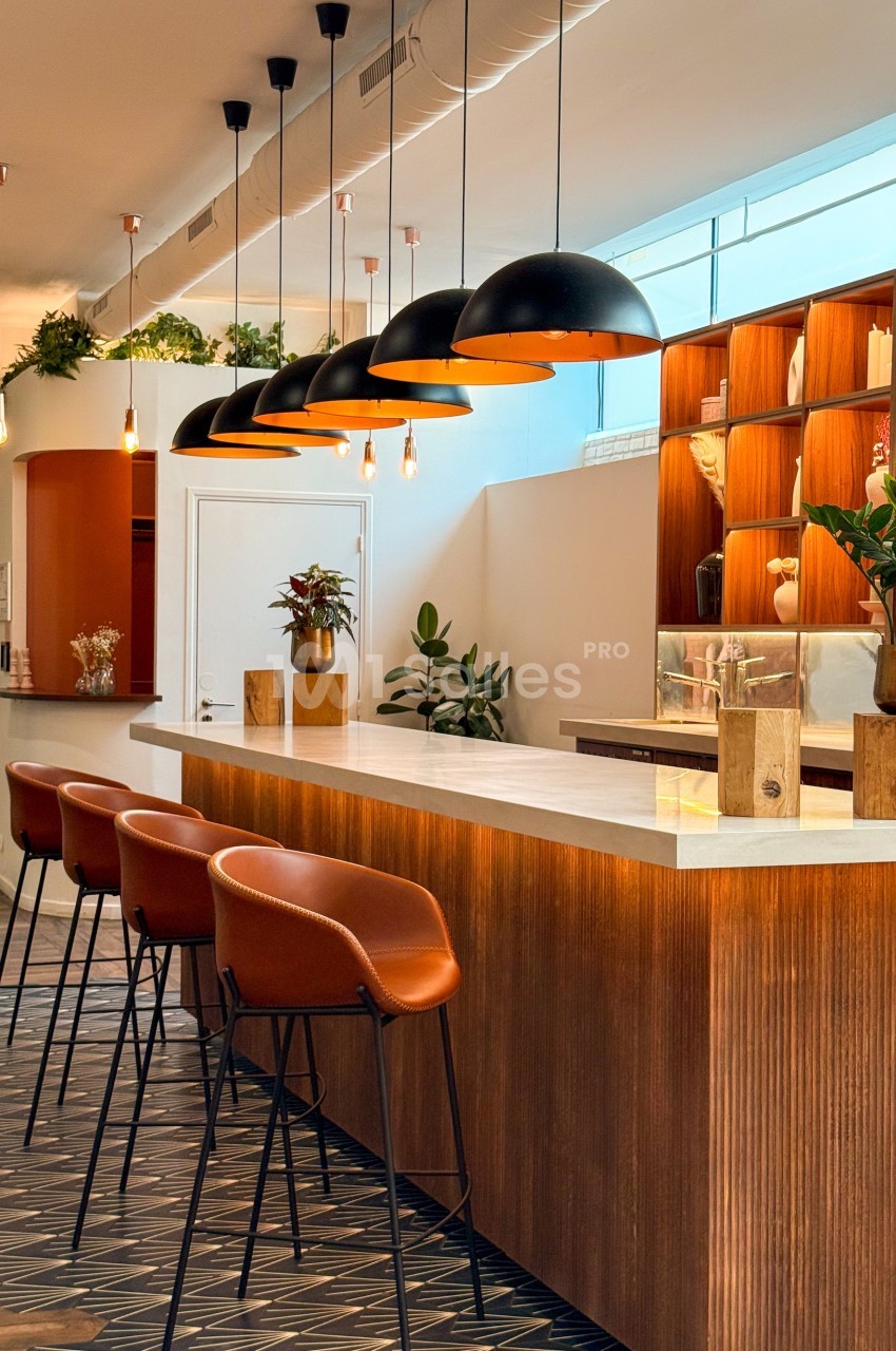 Comptoir en bois avec tabourets orange, luminaires suspendus noirs et étagères décorées dans un espace moderne et lumineux.