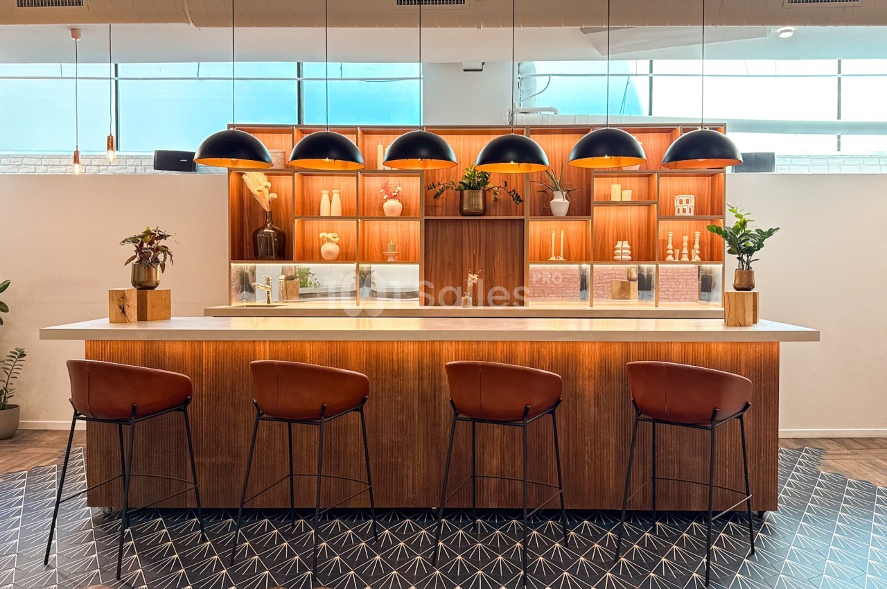 Comptoir en bois avec tabourets, étagères décoratives éclairées et suspensions noires dans un espace moderne et lumineux.