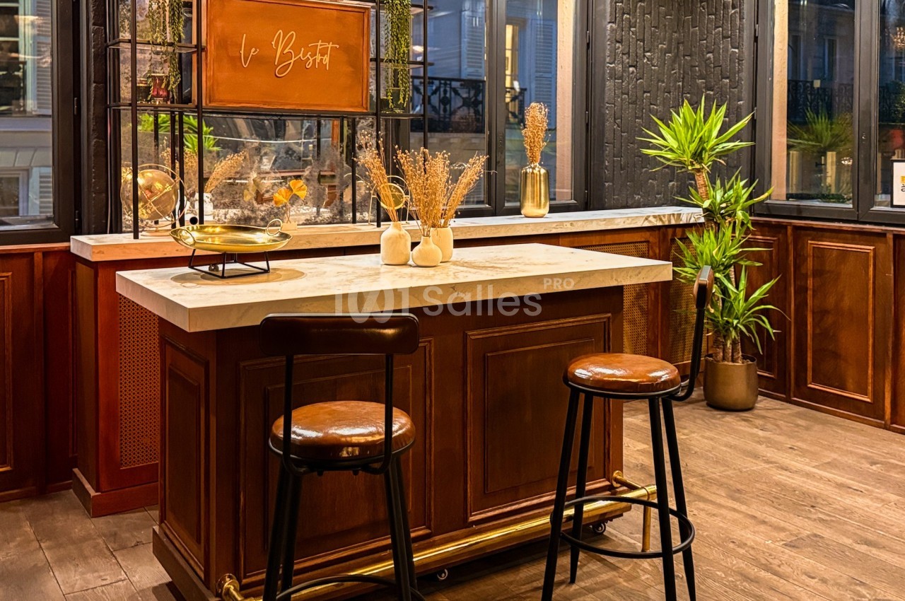 Cuisine moderne avec un îlot central en bois, tabourets hauts, plantes vertes et décoration minimaliste.