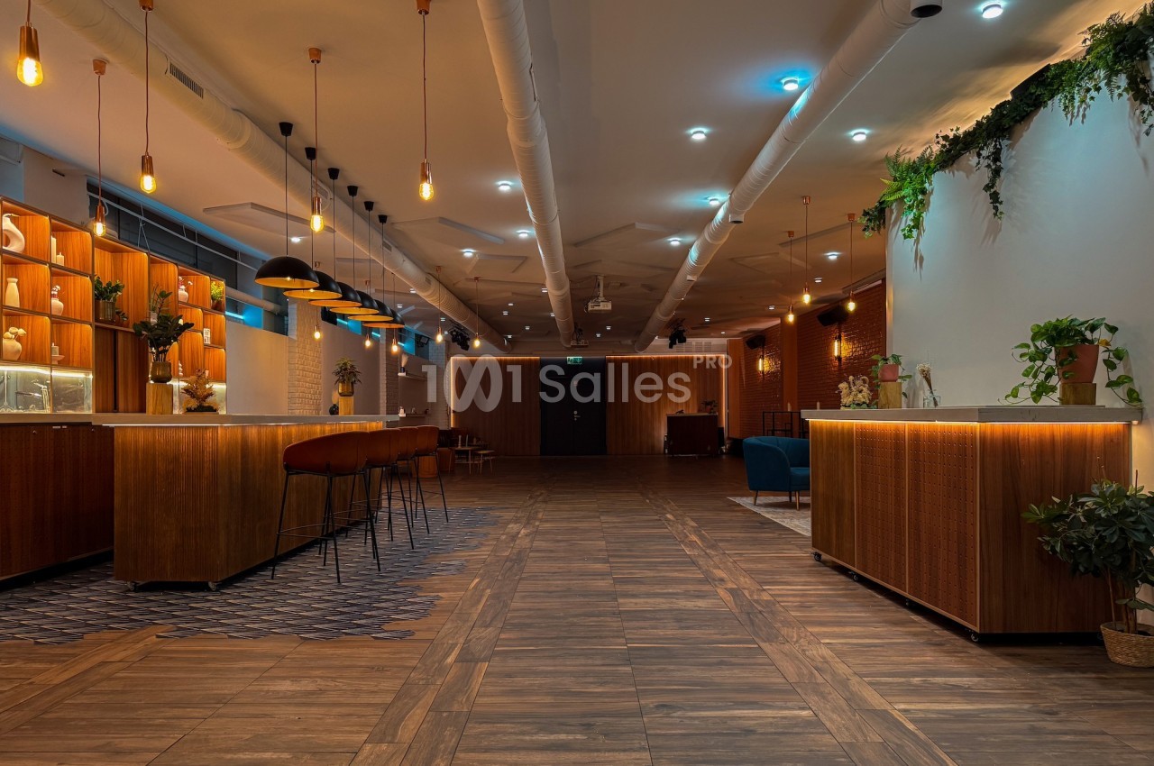 Salle moderne avec éclairage chaleureux, comptoirs en bois, plantes décoratives et sol en parquet.