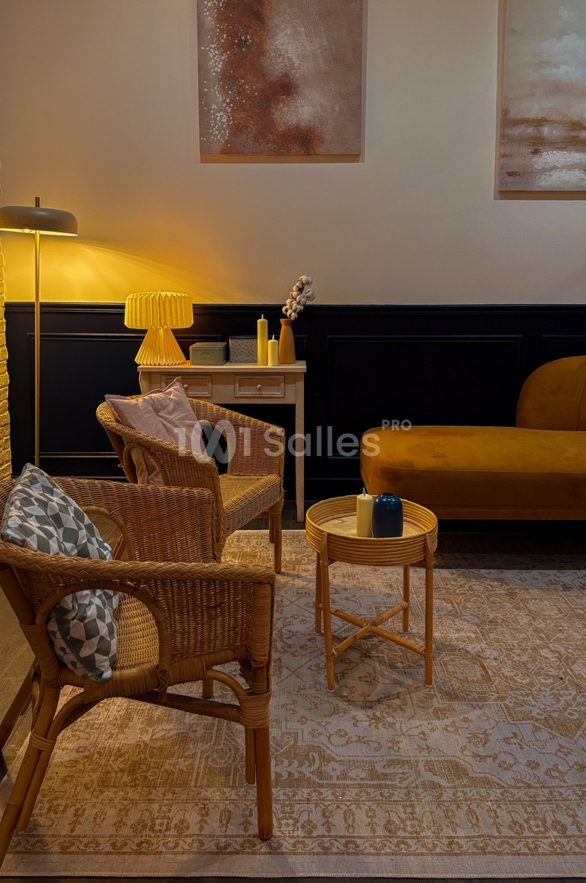 Espace salon cosy avec fauteuils en rotin, table basse, canapé jaune moutarde et éclairage tamisé.