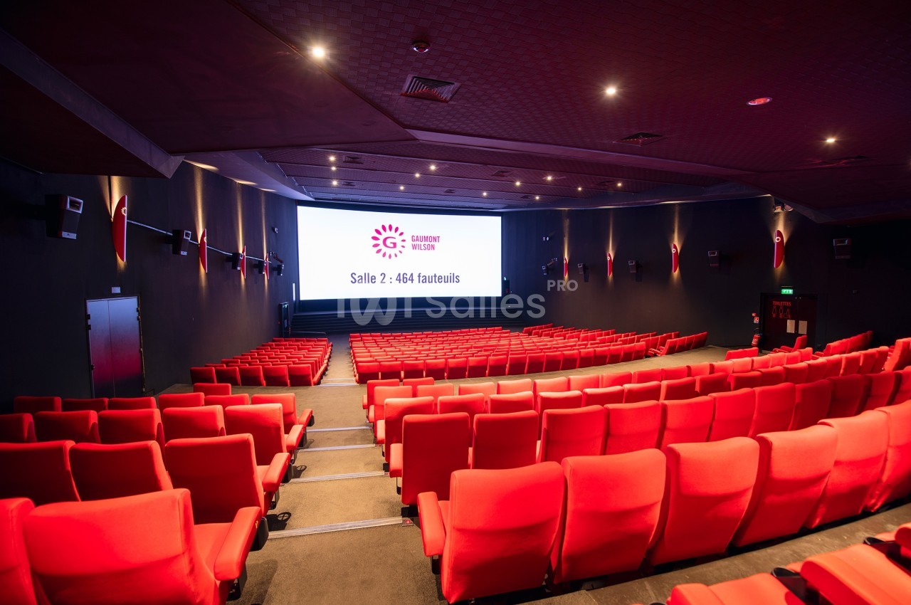 Salle de cinéma moderne avec des rangées de fauteuils rouges et un écran affichant des informations sur la capacité.