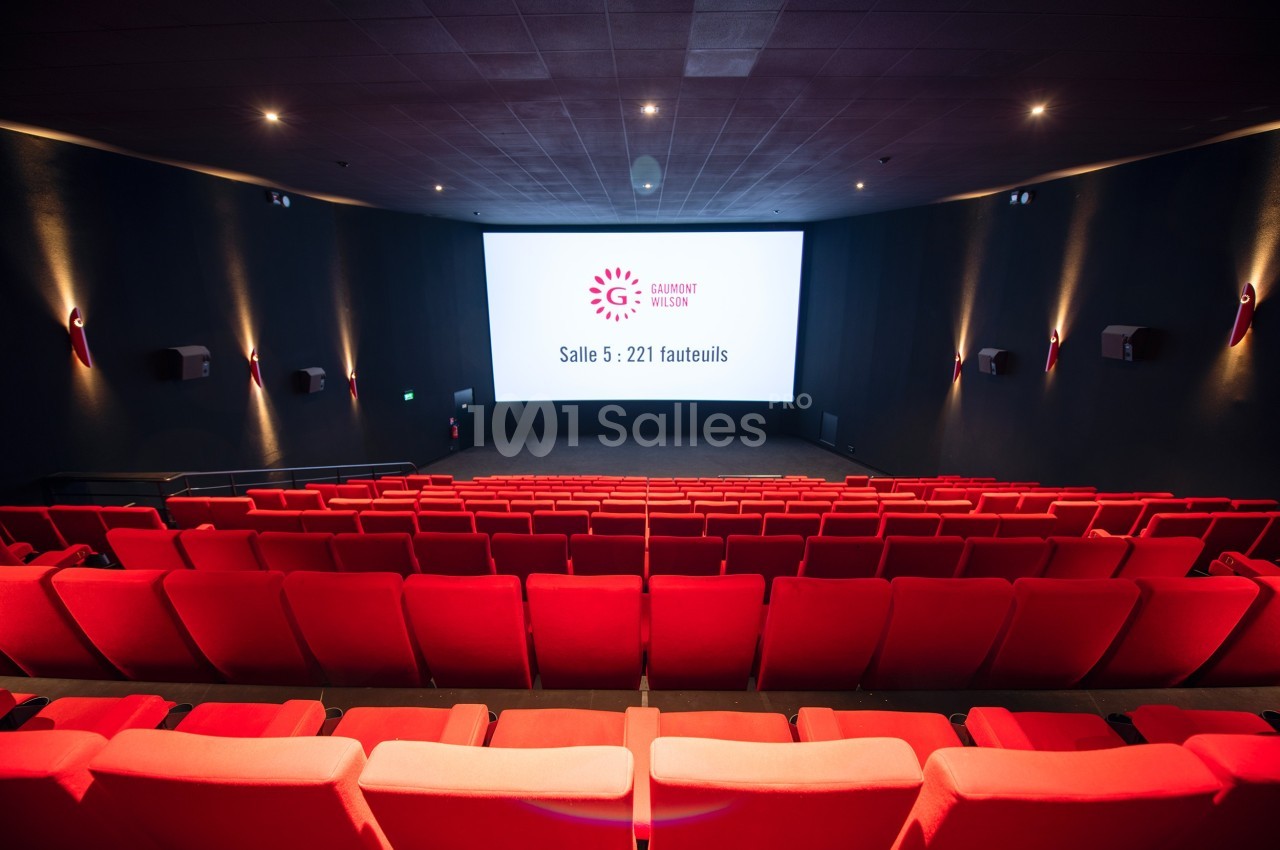 Salle de cinéma vide avec des rangées de fauteuils rouges et un écran affichant ’Salle 5 : 221 fauteuils’.