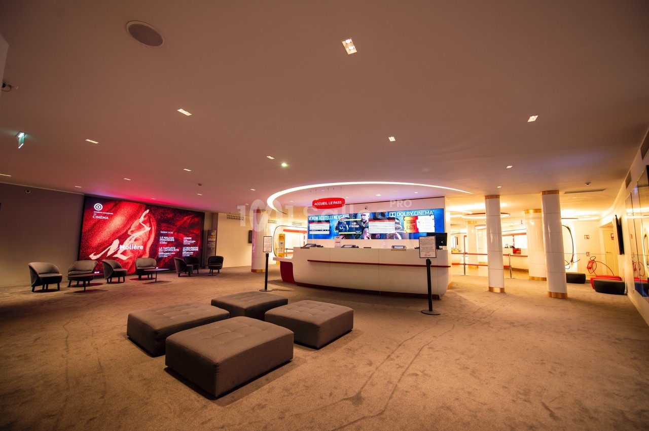 Hall d'accueil spacieux avec comptoir central, sièges, éclairage chaleureux et écrans d'affichage lumineux.