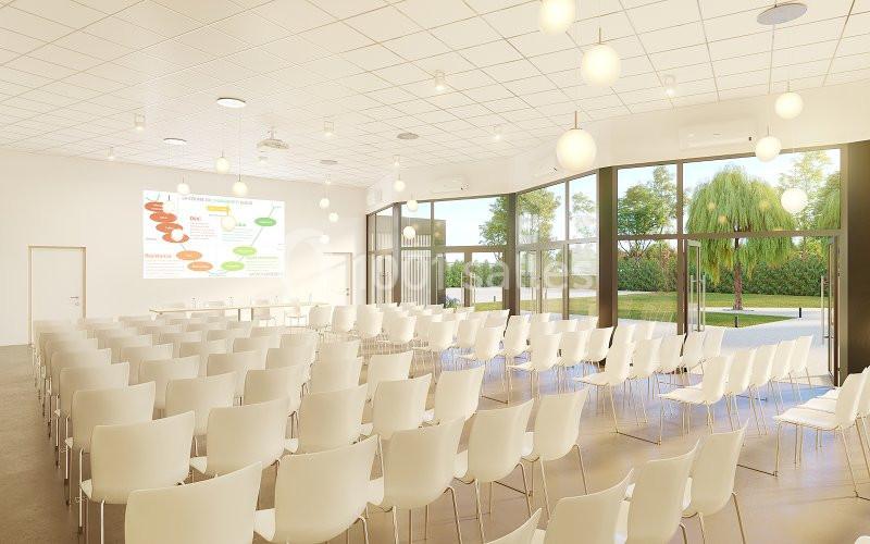 Salle de conférence lumineuse avec des rangées de chaises blanches, grandes baies vitrées et un écran de projection allumé.