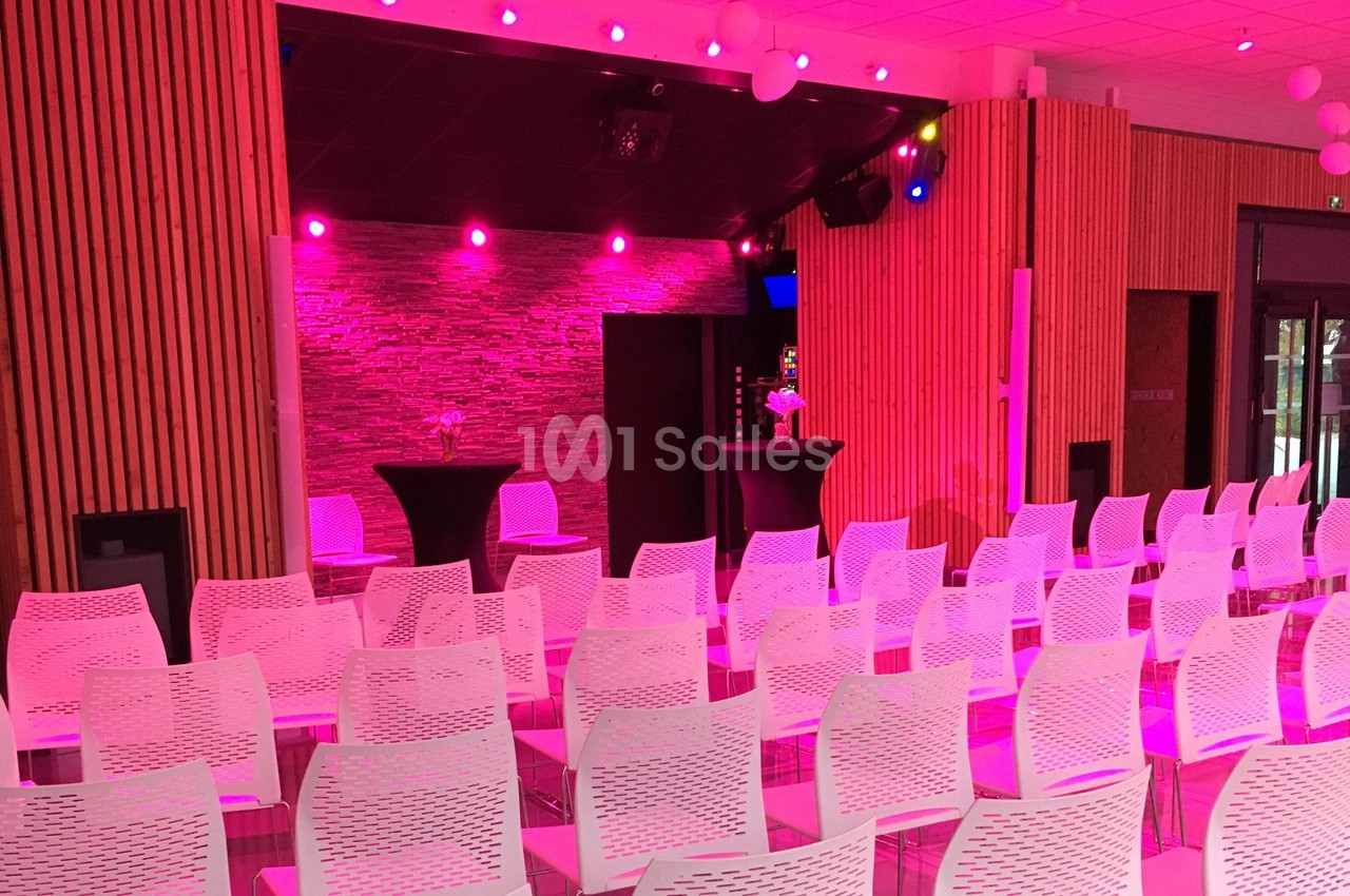 Salle de conférence avec des chaises blanches alignées, éclairage rose et un mur en pierre en arrière-plan.