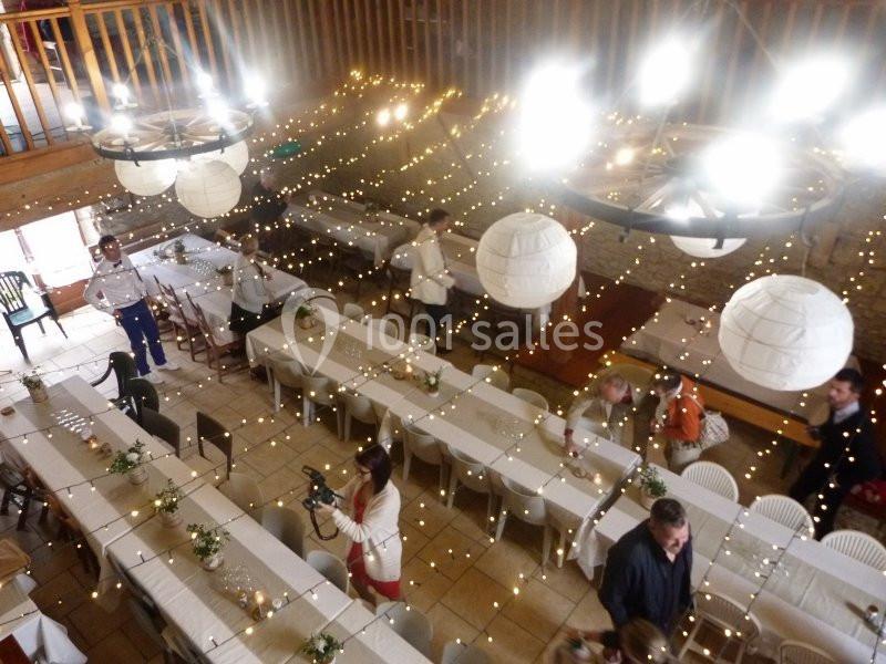 Salle décorée pour un événement avec guirlandes lumineuses, tables alignées et quelques personnes en préparation.