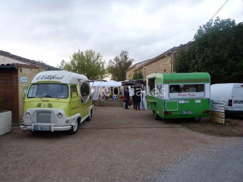 Deux camions-restaurants vintage stationnés sur une place en plein air, avec des stands et des visiteurs en arrière-plan.