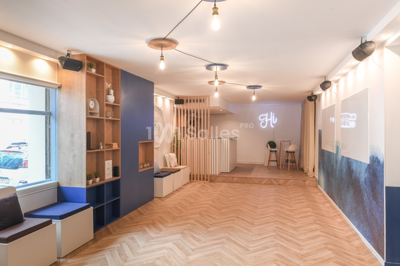 Salle lumineuse avec parquet en bois, mobilier moderne, étagères décoratives et éclairage suspendu.