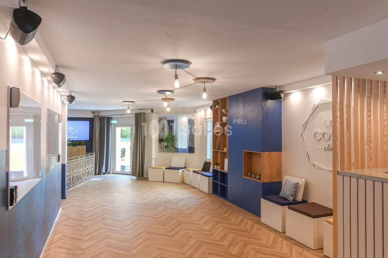 Espace intérieur lumineux avec parquet en chevrons, murs décorés, étagères et assises, éclairé par des suspensions.