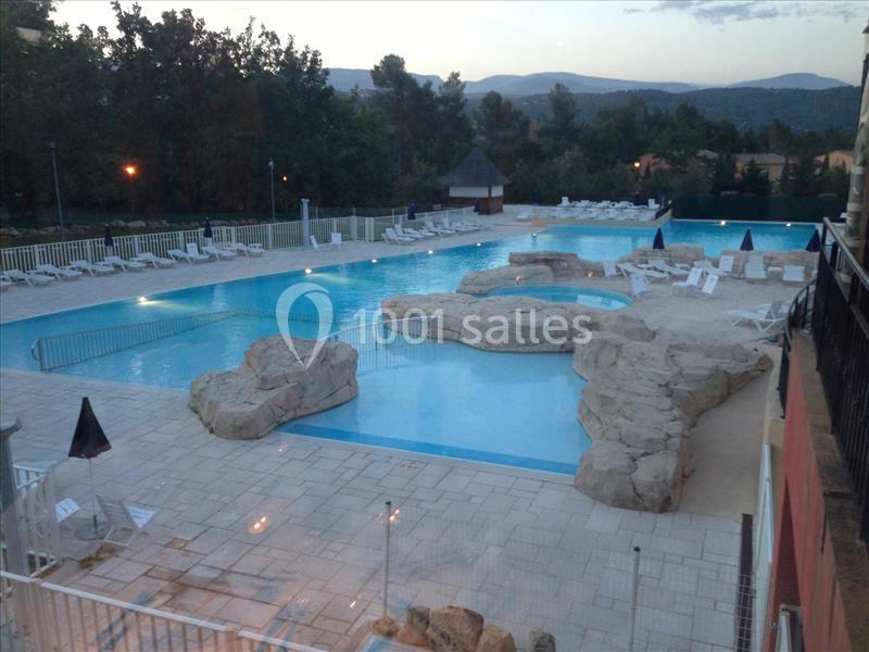 Piscine extérieure avec rochers décoratifs, transats blancs autour et paysage boisé en arrière-plan.