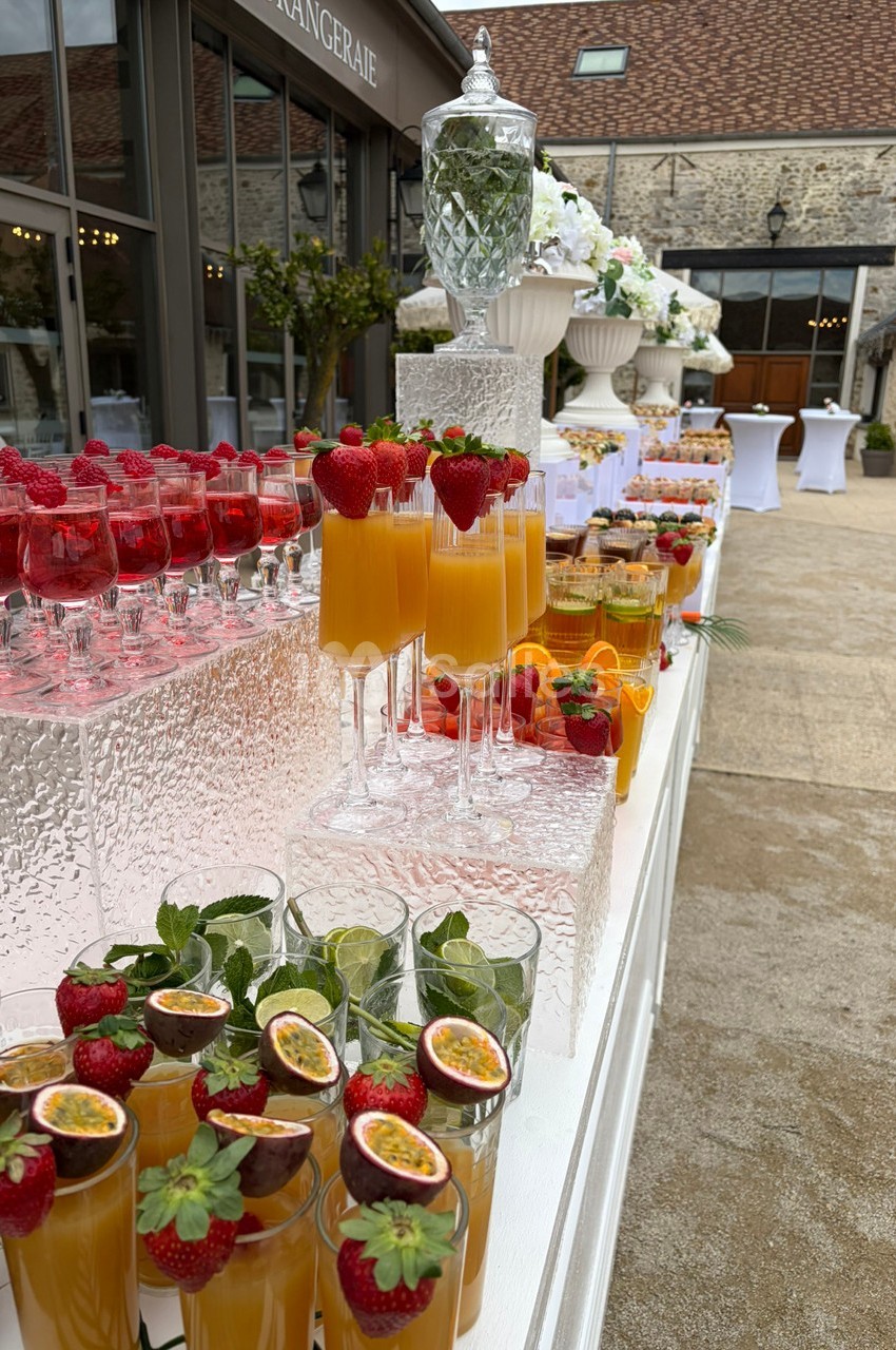 Buffet de cocktails colorés avec fruits frais, disposés sur une table en extérieur près d'un bâtiment en pierre.