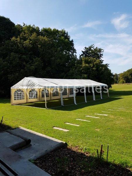 Tente blanche rectangulaire montée sur une pelouse, entourée d'arbres sous un ciel dégagé.