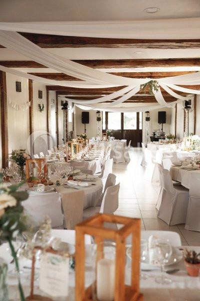 Salle de réception décorée avec des nappes blanches, des guirlandes suspendues et des tables dressées pour un événement.