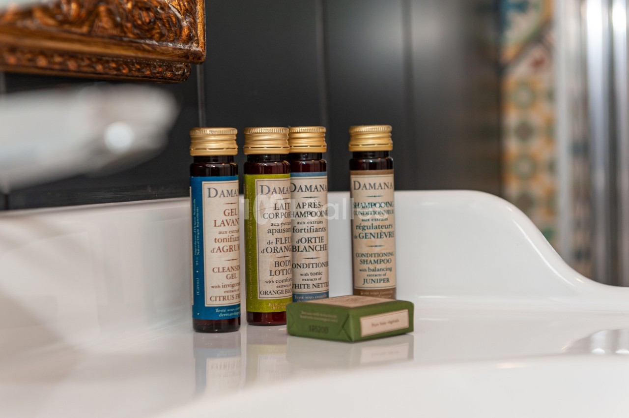 Quatre flacons de produits de toilette et un savon vert posés sur un lavabo blanc.