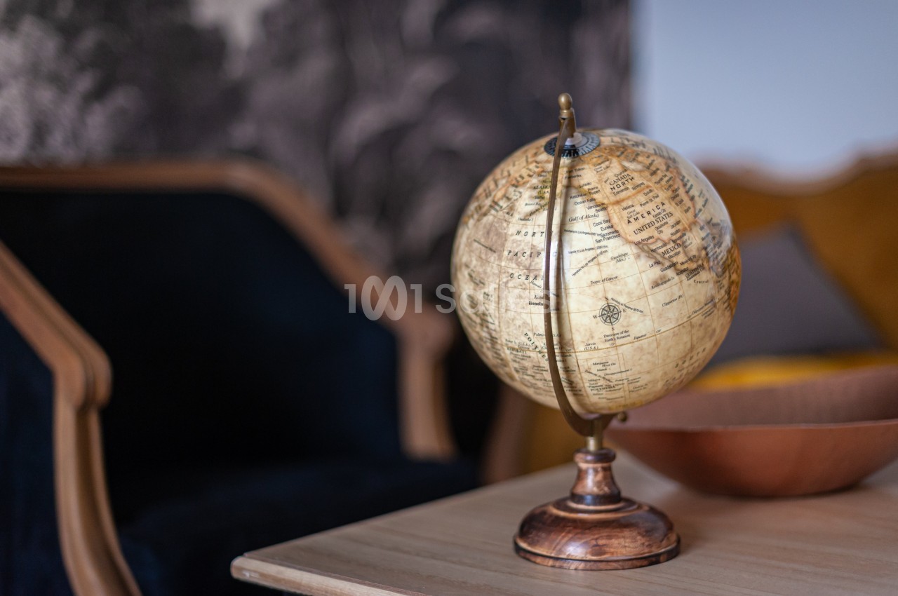 Globe terrestre ancien posé sur une table en bois, avec un fauteuil et un décor sombre en arrière-plan.